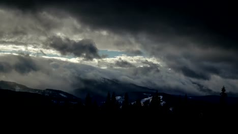 Time-lapse-thunder-clouds-moving-above-winter-mountain-range-dark-pine-forest-foreground-nature-landscape