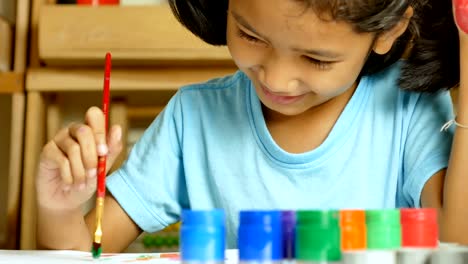 The-little-girl-is-using-a-red-paintbrush-dipped-in-a-colored-bottle-to-paint-on-her-finger.