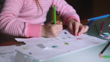 Close-up-shot-of-cute-Caucasian-little-girl-learning-to-draw-on-paper-holding-a-pencil-with-whole-hand-at-home-table