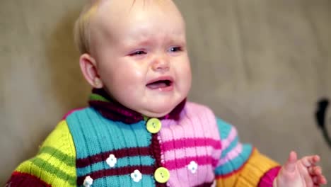 Baby-girl-sitting-in-the-house-and-crying,-clutching-his-head.