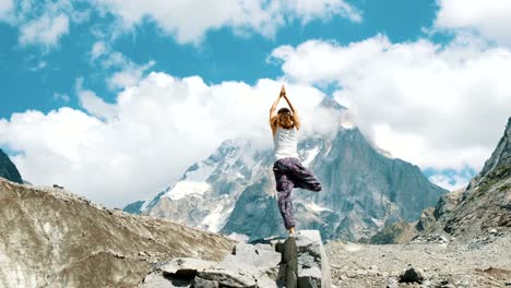 Woman-performs-an-basic-asana-tree---vriksasana-in-yoga-on-a-background-of-a-snowy-mountain-in-a-hike.-Girl-does-gymnastics-on-fresh-air-in-a-hike-on-the-nature