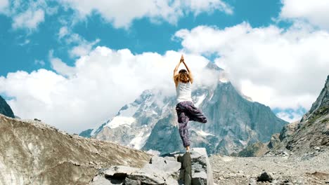 Frau-führt-einen-grundlegende-Asana-Baum---Vriksasana-im-Yoga-auf-einem-Hintergrund-von-einem-schneebedeckten-Berg-in-der-Wanderung.-Mädchen-macht-Gymnastik-an-der-frischen-Luft-bei-einer-Wanderung-auf-die-Natur