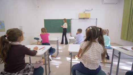 Kinder-Schulbildung,-führt-junge-Lehrerin-Frau-in-der-Nähe-von-Blackboard-kognitive-Lektion-für-kleine-Kinder-am-Schreibtisch-im-Klassenzimmer-der-Schule