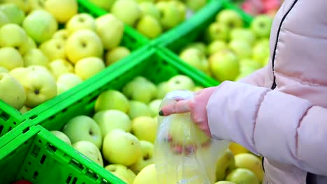 Nahaufnahme-der-Hand-einer-Frau-im-Winter-Kleidung-Puttinggreen-Äpfel-in-einem-Paket.-Sie-wählt-die-leckeren-und-frischen-Früchten.