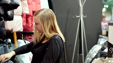 Una-mujer-elige-una-chaqueta-hacia-abajo.-En-la-tienda-de-ropa-de-abrigo