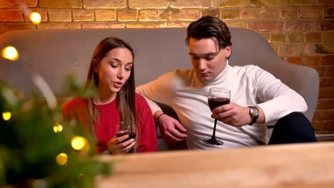 Retrato-de-joven-caucásicos-amigos-sentados-en-el-piso-y-beber-vino-hablando-entre-sí-en-el-acogedor-ambiente-de-Navidad.