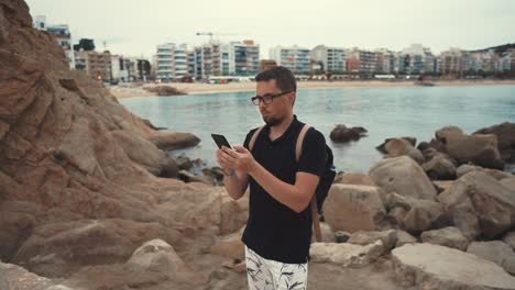 Hombre-en-una-orilla-del-mar-con-un-smartphone.