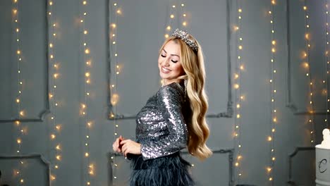 A-blond-woman-in-a-beautiful-dress-and-a-crown-is-posing-in-the-studio.-Red-sofa