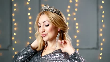 A-blond-woman-in-a-beautiful-dress-and-a-crown-is-posing-in-the-studio.-Red-sofa