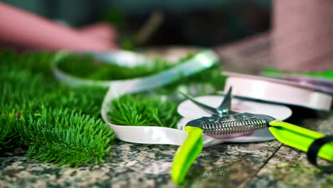 Working-counter-of-a-florist,-scissors,-ribbon-and-fir-branch.