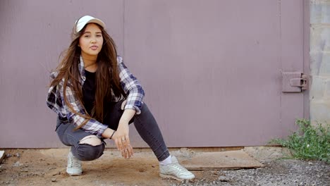 A-young-woman-sits-at-an-iron-gate-and-looks-at-the-camera.