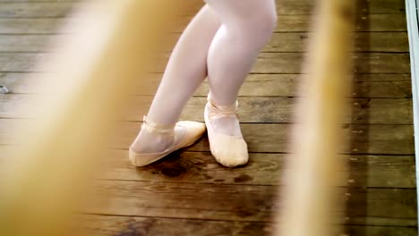 close-up,-in-dancing-hall,-ballerina-performs-pas-soute,-jumping-in-ballet-shoes-near-barre,-on-an-old-wooden-floor,-in-ballet-class