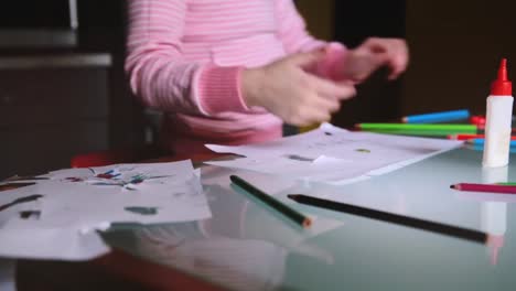 Camera-sliding-right-showing-little-European-girl-child-in-pink-sweater-taking-a-pencil-to-draw-at-table-with-stationery