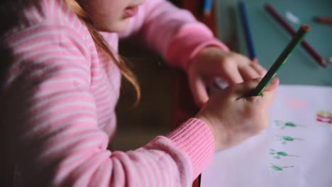 Camera-sliding-right-over-cute-Caucasian-little-girl-drawing-on-paper-with-different-color-pencils-at-a-table-close-up