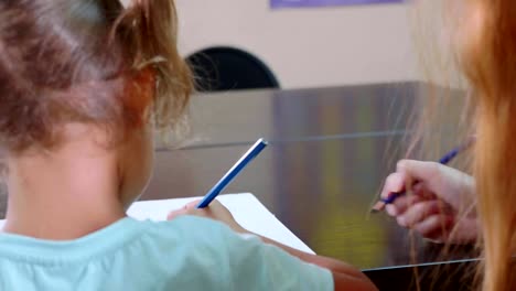 Little-cute-girl-sits-in-classroom-and-studies-with-teacher-in-exercise-book