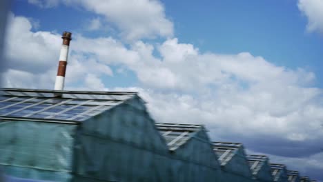 Car-view-tracking-shot-of-large-glass-greenhouses-of-modern-farm-and-blue-sky-with-clouds-above-them