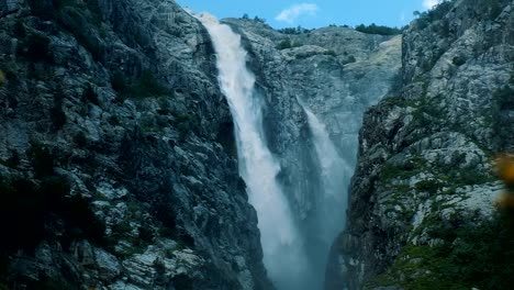 Huge-waterfall-in-the-mountains,-a-powerful-stream-of-water-falls-from-the-rocks,-slow-motion