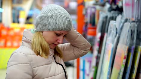 A-middle-aged-woman-in-a-hat-and-a-down-jacket-chooses-goods-in-the-supermarket.