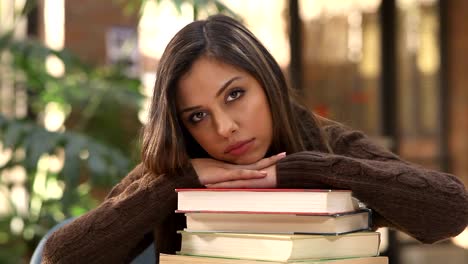 A-college-student-rests-her-head-on-her-text-books-and-smiles