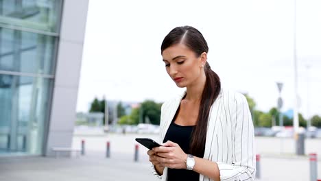 Schöne-Geschäftsfrau-mit-Telefon-während-des-Gehens-in-der-Nähe-von-Office