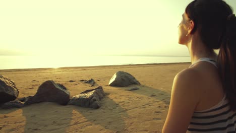 Active-young-woman-streching-and-practicing-yoga-on-beach-at-sunset.