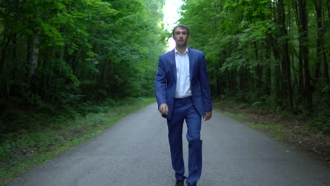 young-businessman-in-a-blue-suit-is-walking-along-the-road-in-forest