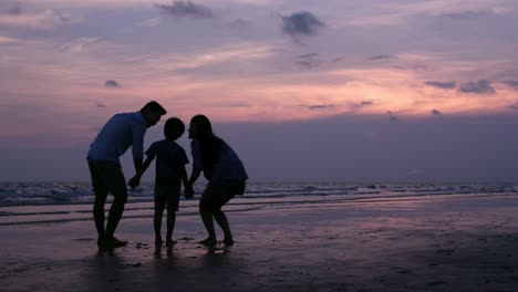 SLOW-MOTION,-familia-asiática-silueteado-mirando-al-atardecer-con-feliz-emoción-en-la-playa-juntos.-Concepto-de-familia,-vacaciones-y-viajes.