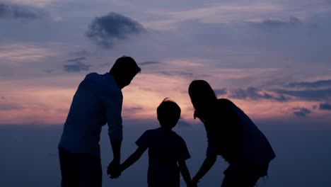 SLOW-MOTION,-Silhouetted-Asian-family-looking-to-sunset-with-happy-emotion-at-Beach-together.-Family,-Holiday-and-Travel-concept.