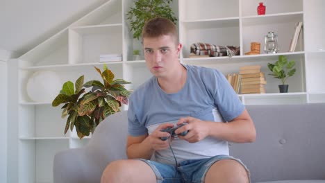 Closeup-portrait-of-adult-attractive-caucasian-man-playing-video-games-using-game-console-being-nervous-sitting-on-couch-indoors