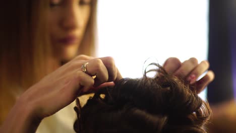 Young-blonde-stylist-girl-makes-hairstyle-to-a-woman