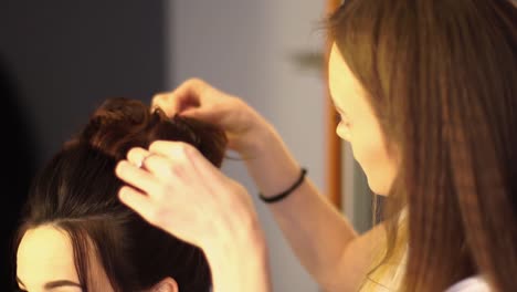 Young-blonde-stylist-girl-makes-hairstyle-to-a-woman