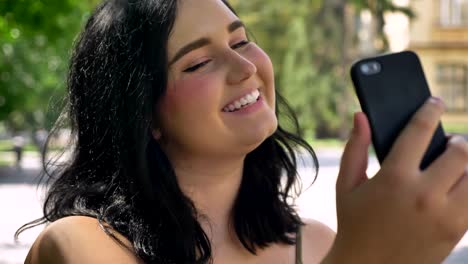 Retrato-de-joven-bella-mujer-con-obesidad-tomando-selfie-con-su-teléfono,-sonriendo-y-de-pie-en-la-calle-en-el-parque,-feliz