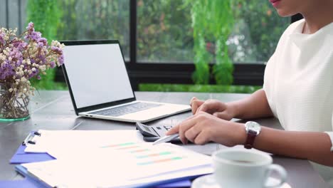 Hermosa-joven-sonriente-mujer-asiática-trabajando-en-ordenador-portátil-mientras-está-sentado-en-la-sala-de-estar-en-casa.-Mujer-de-negocios-asiática-de-trabajo-finanzas-documentos-y-calculadora-en-su-oficina-en-casa.-Disfrutando-en-casa.