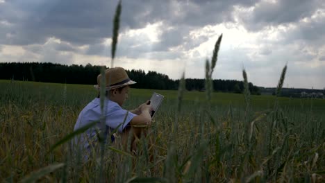 boy-sits-in-a-field-against-beautiful-clouds-and-uses-a-tablet-in-the-evening,-outdoors