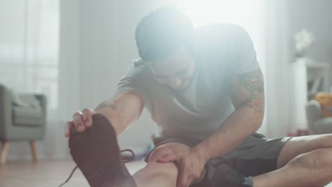 Strong-Athletic-Fit-Man-in-T-shirt-and-Shorts-Stretches-His-Body-for-Morning-Exercises-at-Home-in-His-Spacious-and-Bright-Living-Room-with-Minimalistic-Interior.