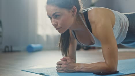 Strong-schöne-Fitness-Girl-in-Athletic-Trainingskleidung-macht-eine-Planke-Übung-beim-verwenden-eine-Stoppuhr-auf-ihrem-Telefon.-Sie-ist-zu-Hause-in-ihrem-Wohnzimmer-mit-gemütlichen-Innenraum-Training.