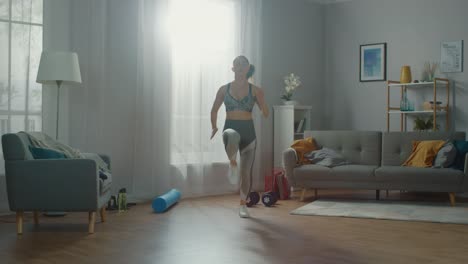 Strong-and-Beautiful-Athletic-Fitness-Girl-in-Workout-Clothes-is-Doing-Energetically-Jogging-in-Place-in-Her-Bright-and-Spacious-Living-Room-with-Minimalistic-Interior.