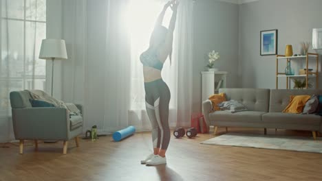 Hermosa-chica-de-Fitness-bien-proporcionado-en-un-Top-deportivo-está-haciendo-estiramientos-ejercicios-de-Yoga-en-su-brillante-y-amplia-sala-de-estar-con-Interior-moderno.