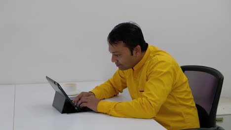 Man-working-on-a-table-with-his-touch-screen-keyboard-tablet-and-receives-a-call-on-his-smart-phone,-takes-it-and-smiles