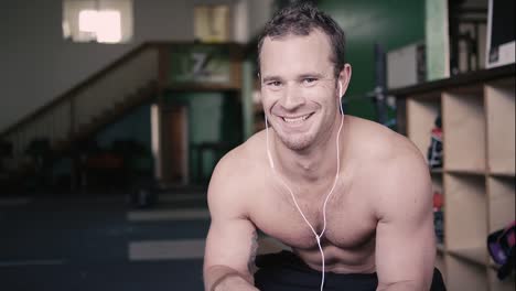 Una-forma-de-hombre-joven-sentada-en-un-gimnasio-toma-una-bebida-de-una-botella-de-agua-y-luego-sonrisas-en-la-cámara