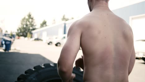 A-fit-young-man-doing-a-tire-flip-outside-of-a-small-gym