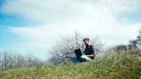 Transportwagen-Schuss.-Mann-mit-Bart-mit-Laptop-auf-Natur-in-der-Nähe-von-blühenden-Baum