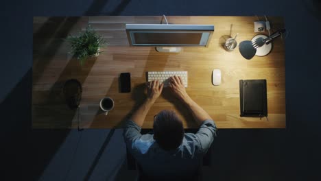 Top-View-of-a-Programmer-Writing-Code-on-His-Personal-Computer-at-Night.-Table-Light-Turned-On.