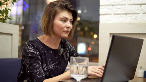 Young-business-woman-sitting-in-a-cafe-with-a-laptop,-working-and-drinking-water