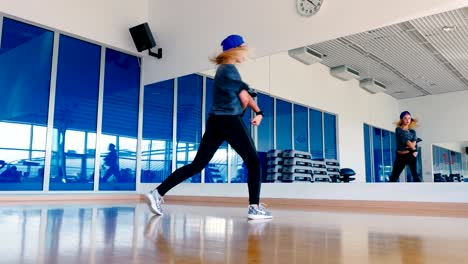 Sporty-girl-in-cap-dancing-in-front-of-mirror-in-gym