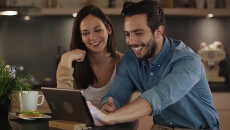 Feliz-pareja-utiliza-Tablet-mientras-sentado-en-la-mesa-de-la-cocina.