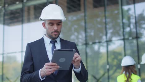 Hombre-de-negocios-en-Hard-Hat-caminando,-hablando,-y-usando-Tablet-Computer.-Edificio-de-cristal-o-rascacielos-en-construcción-en-segundo-plano.