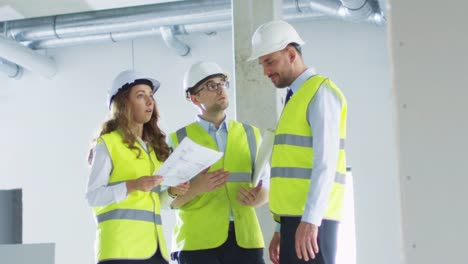 Equipo-de-ingenieros-en-sombreros-duros-teniendo-conversación,-mirando-Blueprint,-dentro-del-edificio-en-construcción.