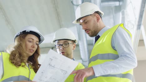 Equipo-de-ingenieros-en-sombreros-duros-teniendo-conversación,-mirando-Blueprint,-dentro-del-edificio-en-construcción.