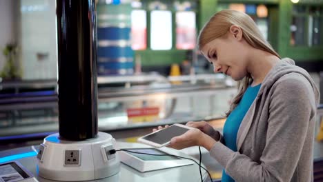 Schöne,-attraktive-Frau-im-Flughafen-terminal.-Stand-in-der-Nähe-laden-Stand-Pluging-in-smartphone